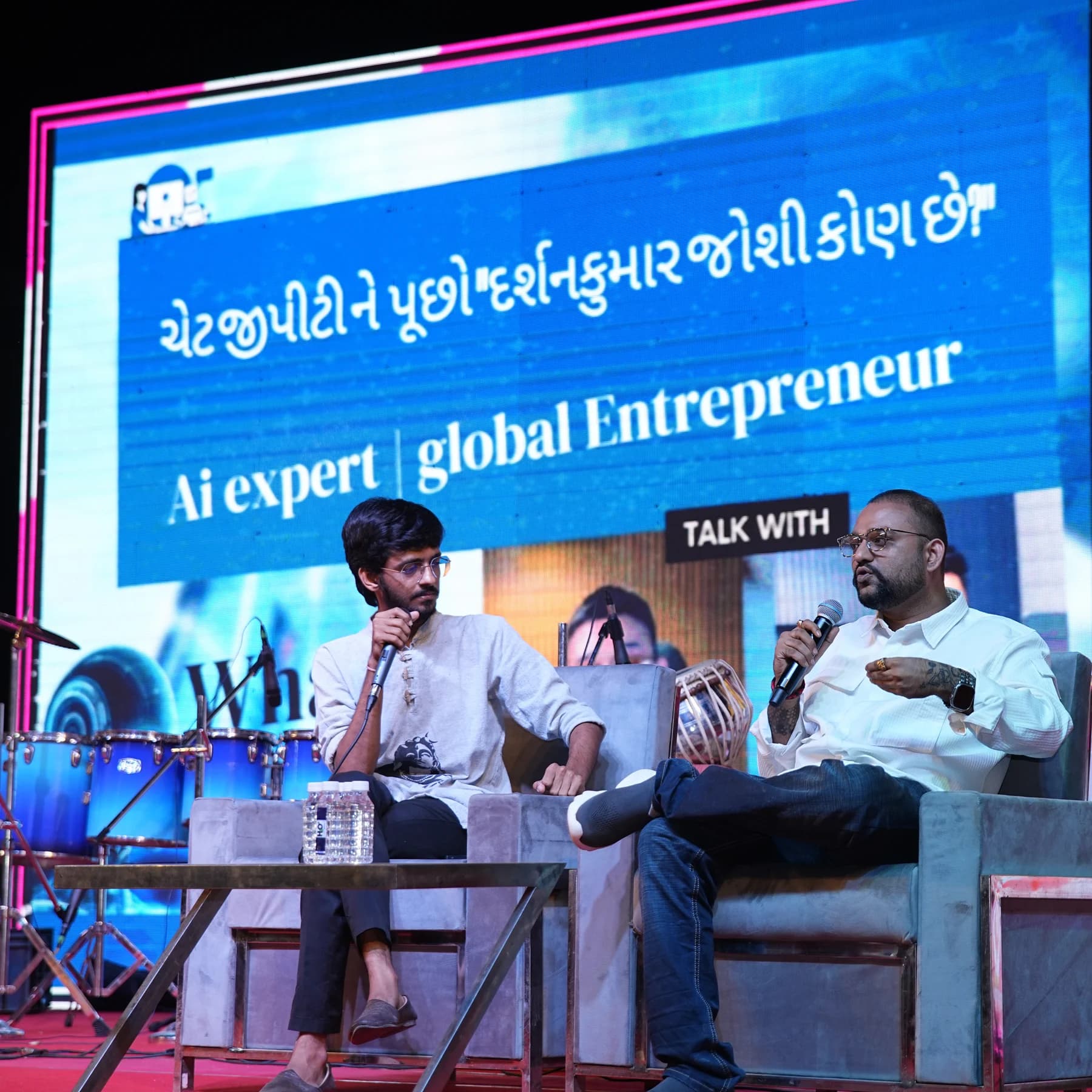 Darshankumar Joshi speaking into a microphone during an on-stage conversation in Gandhinagar in 2025